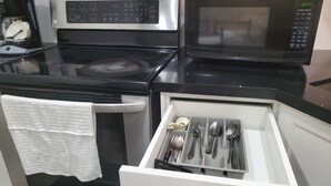 Una cocina con microondas, estufa y un cajón con utensilios.