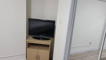 A room with a flat-screen TV on a wooden stand, a white door, and a light-colored wooden floor.