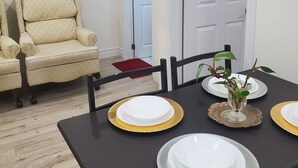 Un comedor con una mesa preparada para cuatro personas, sillas y una silla al fondo.