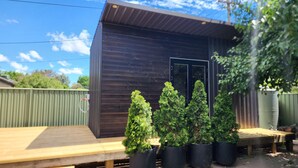 A wooden deck with potted coniferous trees, a metal shed, and a green fence. - Enchanting Tiny Home in Vibrant Dickson (Dickson)