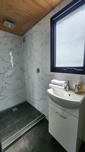 A bathroom with marble tiles, a sink with a mirror, and a shower area.
