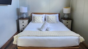 A neatly made bed with a wooden headboard, two bedside tables with lamps, a ceiling fan, and an air conditioning unit. - Enchanting Tiny Home in Vibrant Dickson (Dickson)