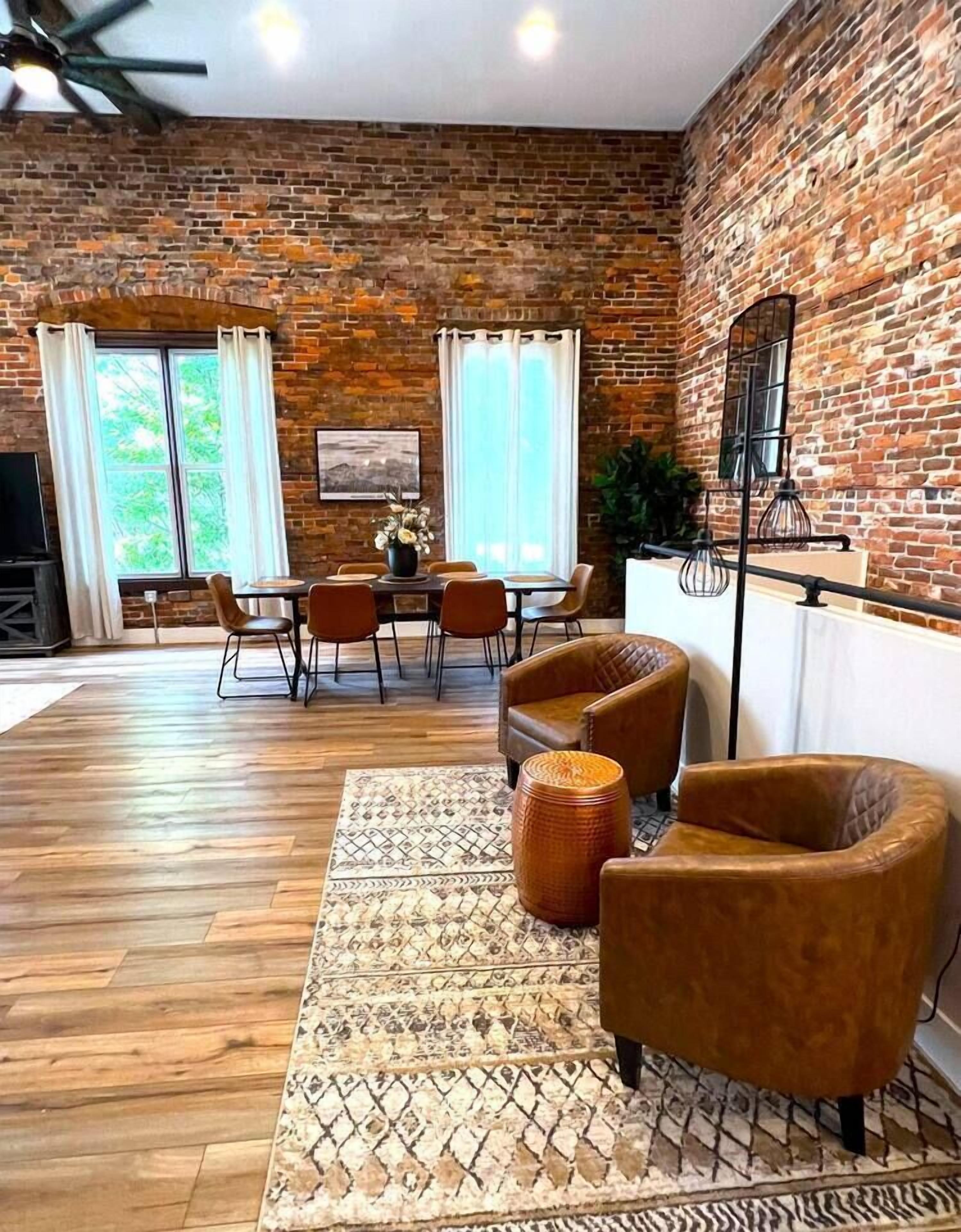 A spacious room with a brick wall, a dining area with chairs and a table, and a seating area with sofas and a patterned rug.