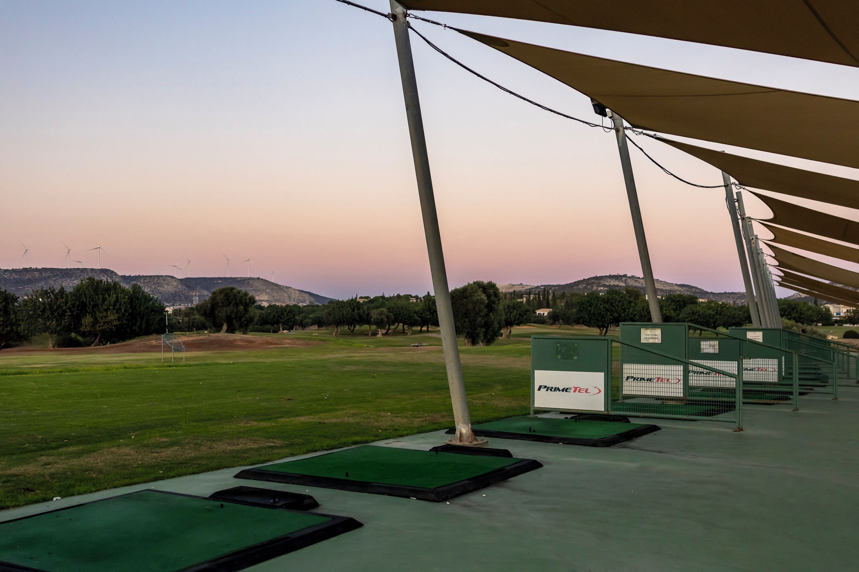 Un parcours d’entraînement au golf avec des tapis verts, des éoliennes et une chaîne de collines en arrière-plan.