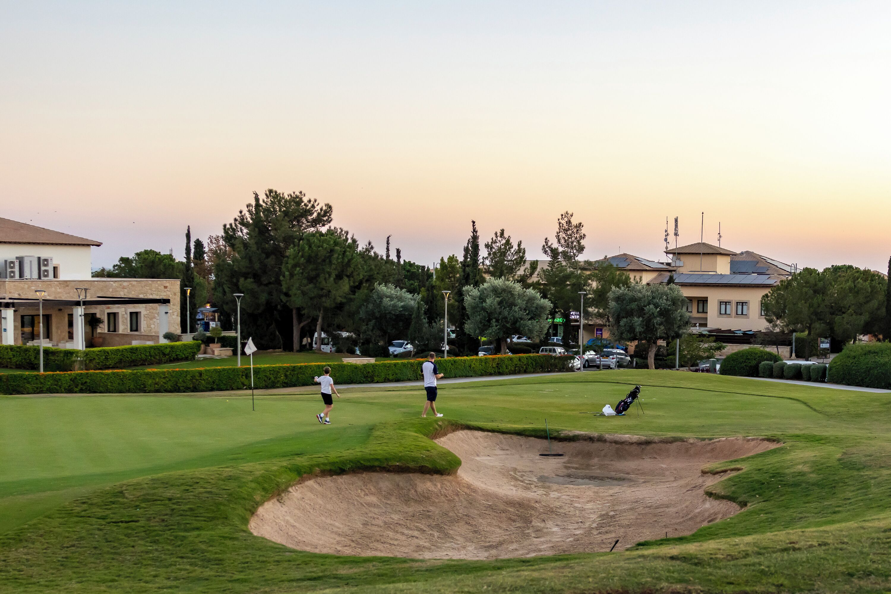 A golf course with sand bunkers, trees, and buildings in the background.
