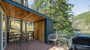 A covered outdoor deck with wooden flooring, metal chairs, and a barbecue grill. - The Golden Nugget Cabin (Keystone)