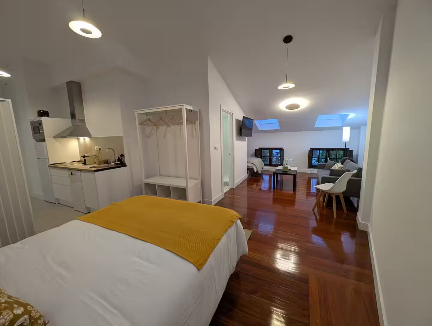 A modern hotel room with a bed, a kitchenette, a seating area, and a view of the sky through skylights.