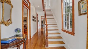 Un pasillo con suelo de madera, una escalera con barandilla de madera y un ventanal grande a la derecha.