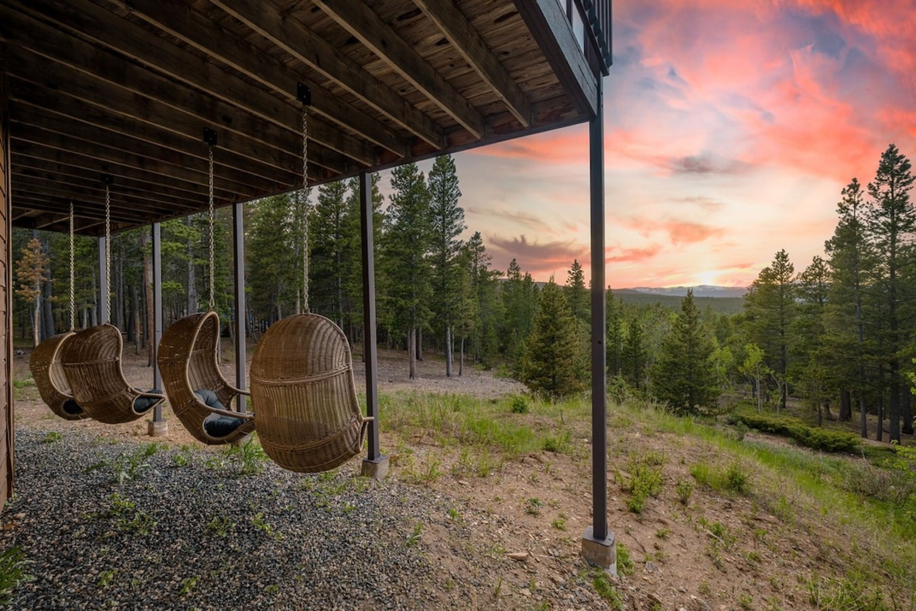 Un área de estar al aire libre techada con sillas de mimbre y vistas a un bosque y al atardecer.