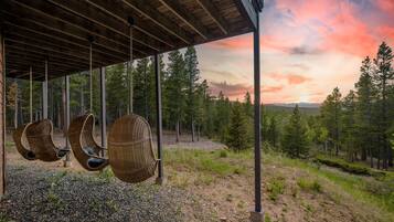 Un área de estar al aire libre techada con sillas de mimbre y vistas a un bosque y al atardecer.