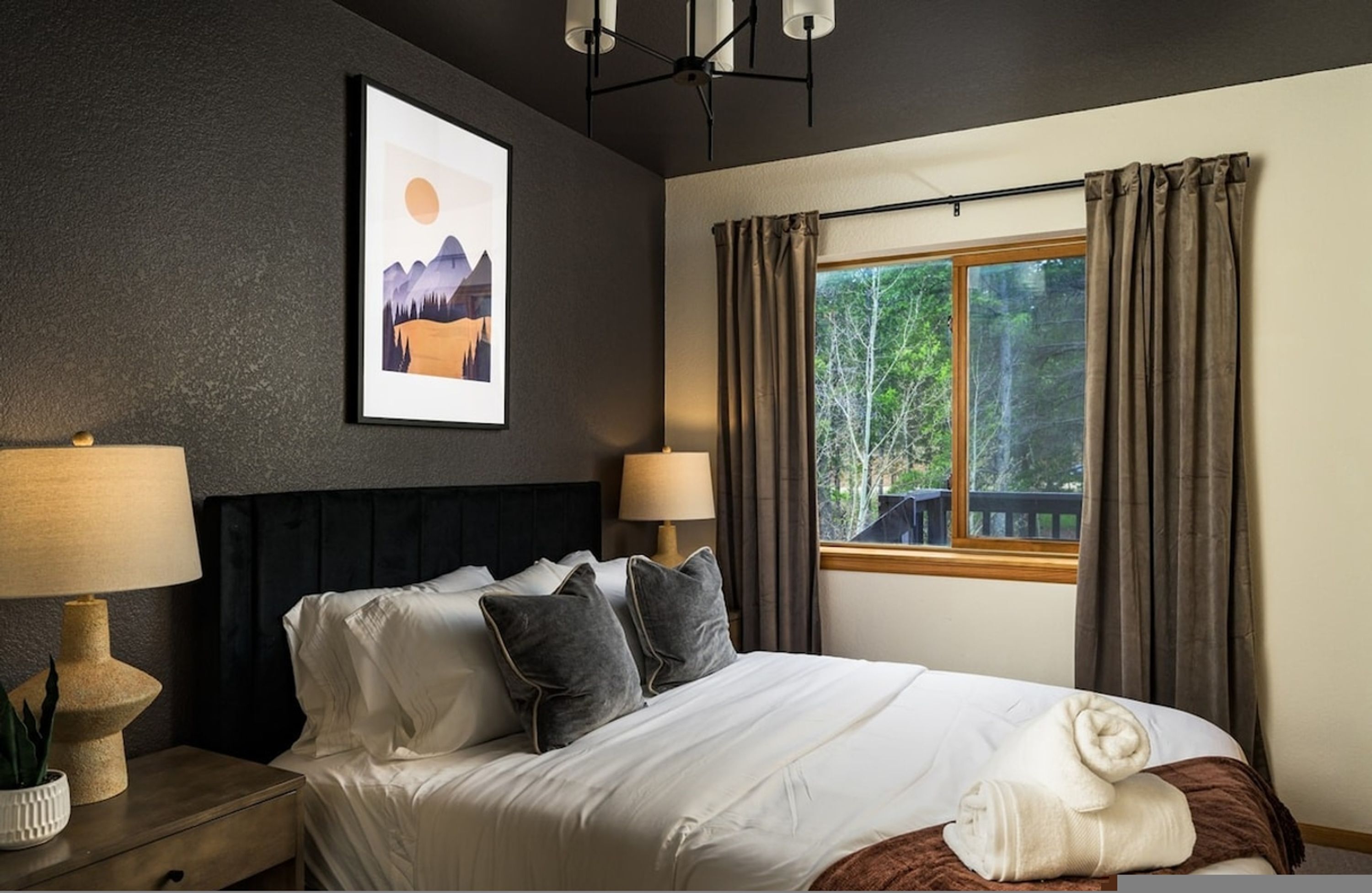 A neatly made bed with pillows, a bedside lamp, a framed picture on the wall, and a window with curtains.