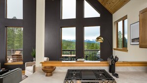 A modern kitchen with a large island, a gas stove, and a view of mountains through large windows. - Serene Retreat Amazing Views Hottub Sauna Xbox (Black Hawk)