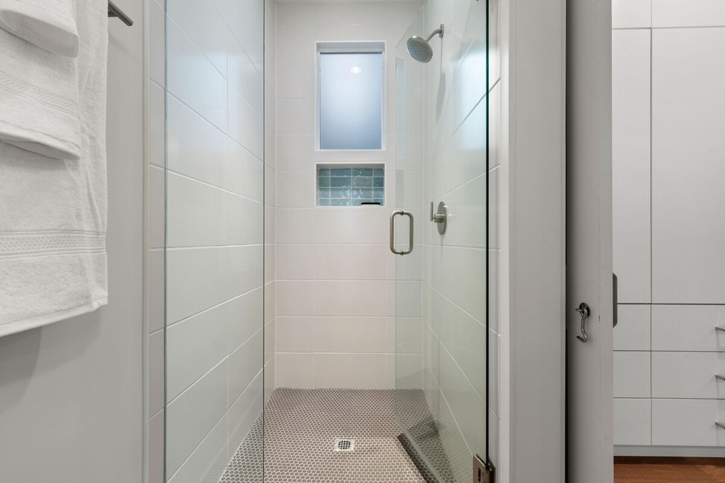 A modern bathroom with a glass shower enclosure, a small window, and a tiled floor.