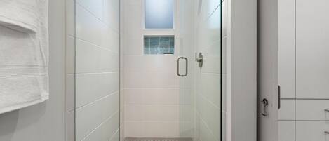 A modern bathroom with a glass shower enclosure, a small window, and a tiled floor.