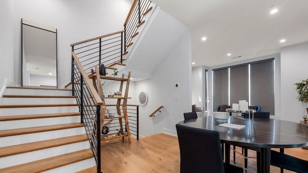 A modern interior with a staircase, a dining area with a round table, and a large window.
