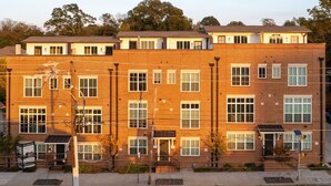 A multi-story brick building with multiple windows, a visible entrance, and a fenced area with trees.