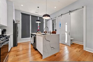 Una cucina moderna con isola centrale, pavimento in legno e illuminazione a sospensione.