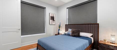 Un dormitorio con cama, mesita de noche, lámpara, un cuadro en la pared y una puerta.