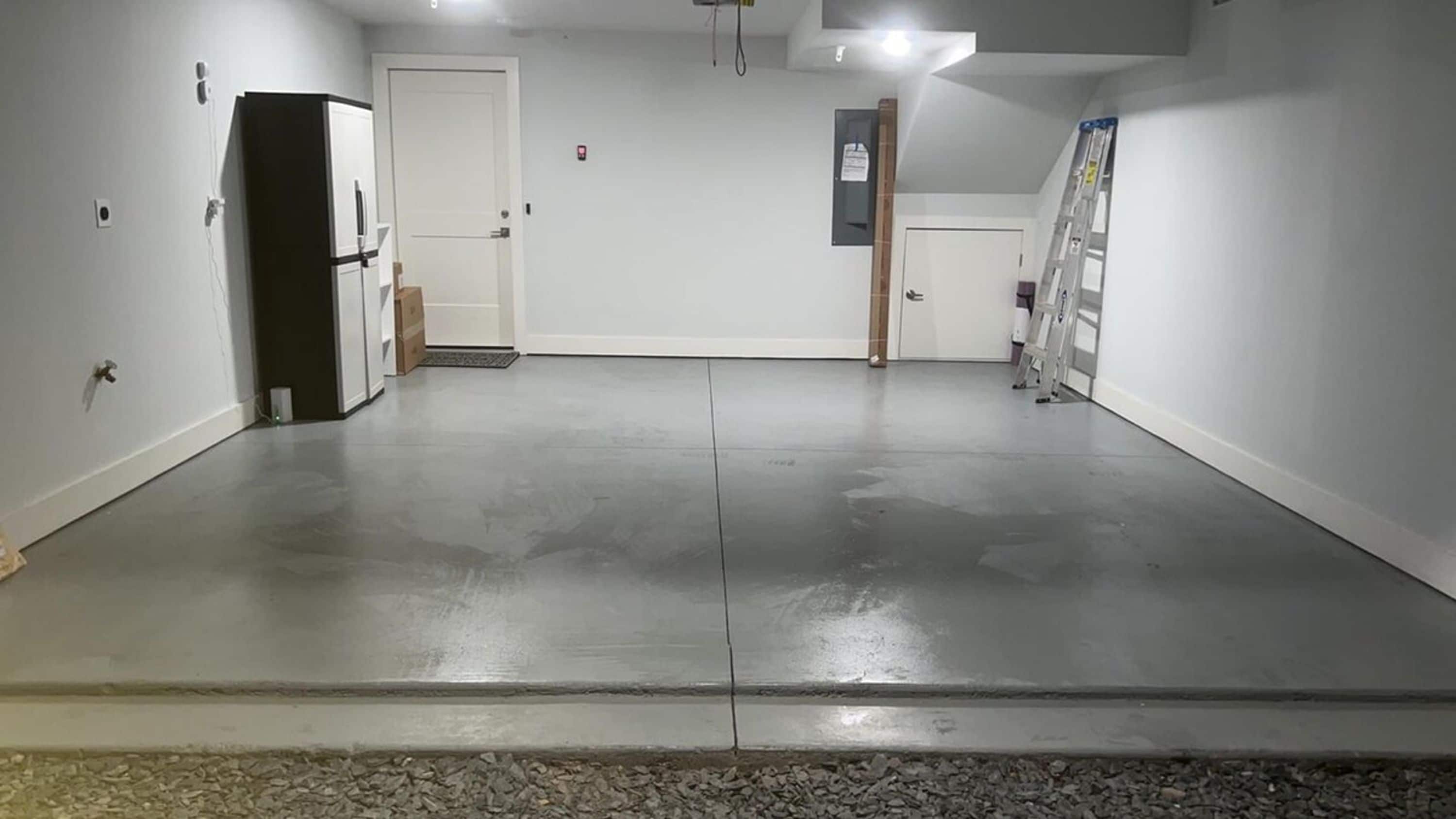Un garage propre et vide, avec un sol en béton, des murs blancs et une porte donnant sur une autre pièce.