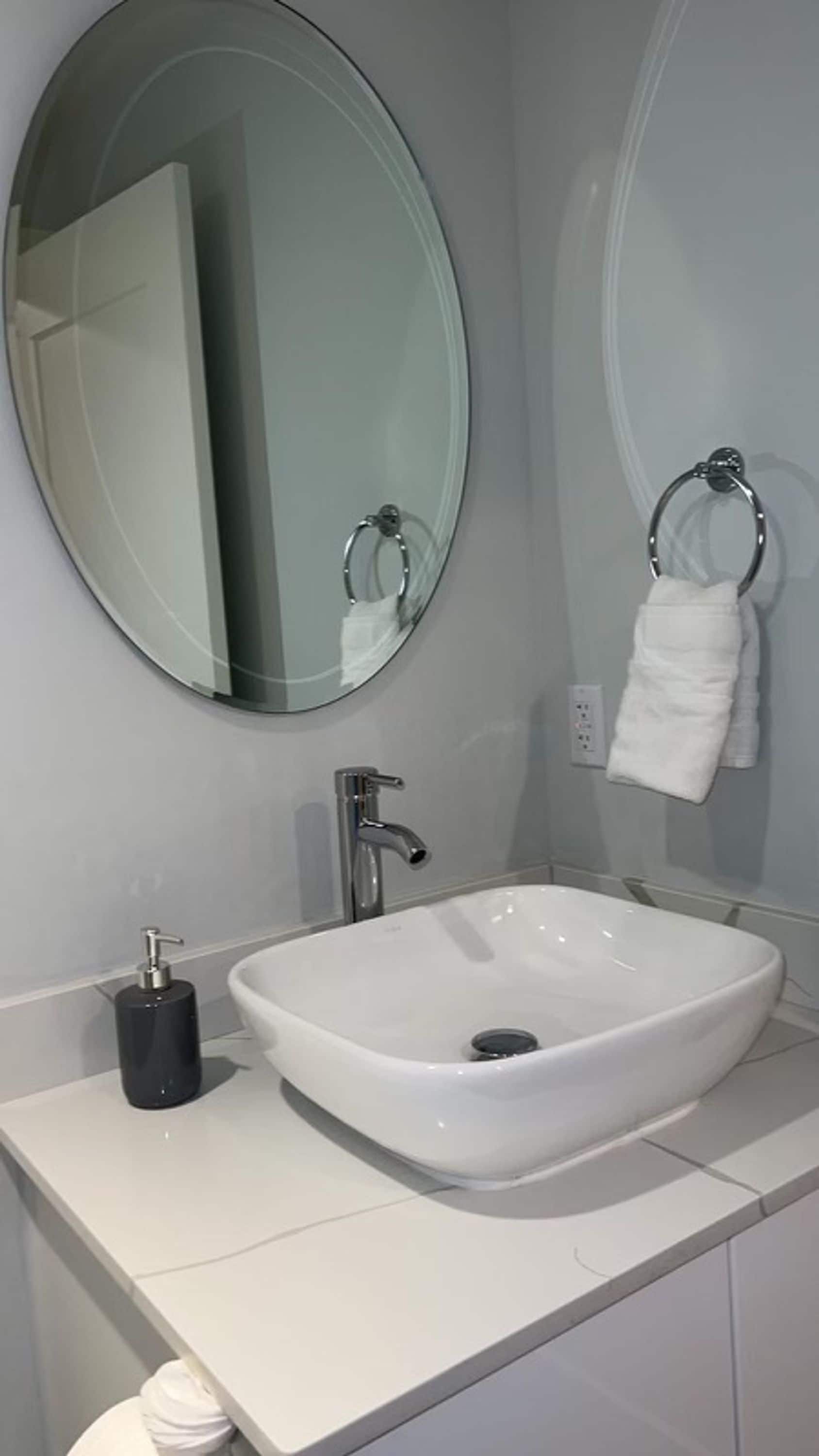 A bathroom with a white sink, a round mirror, and a towel rack.
