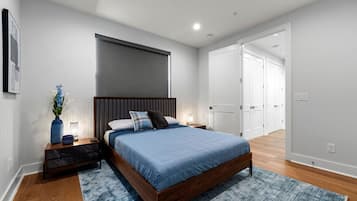 Un dormitorio con cama, mesitas de noche, un cabecero fijado a la pared, una puerta y un pasillo.