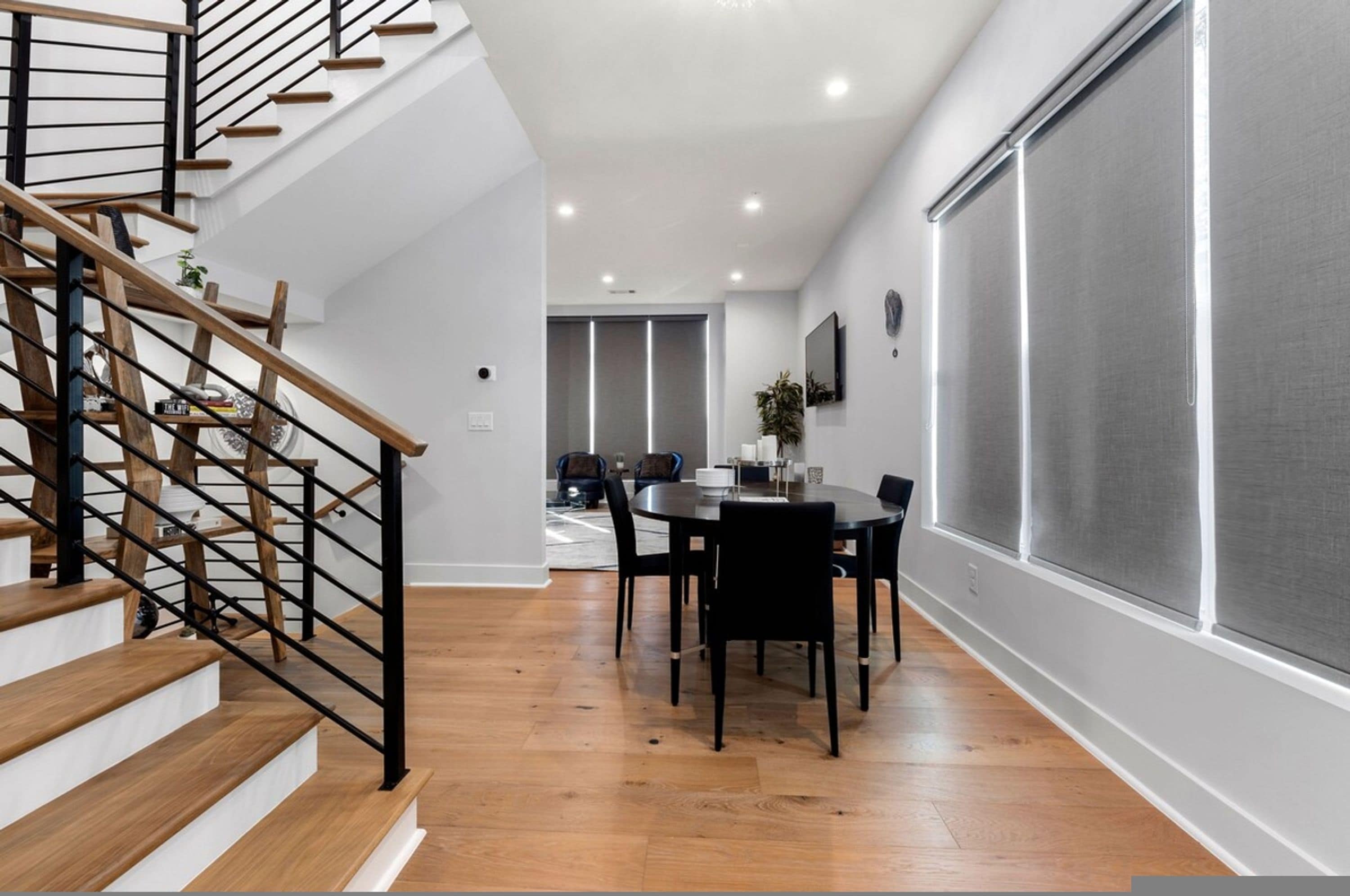 A modern interior with a staircase, dining area, and large windows.