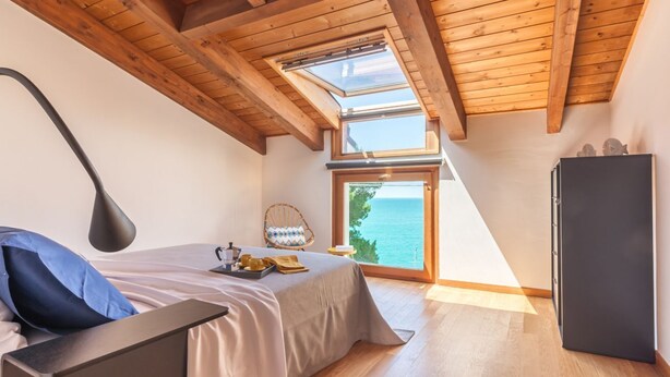 Un dormitorio con cama, escritorio, silla, armario y vista al mar.