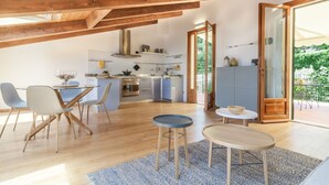 Una cocina moderna con vigas de madera, una zona de comedor con una mesa redonda y vistas a espacios verdes.