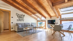 Una sala de estar moderna con techo de madera, un sofá, una mesa de comedor con sillas y un ventanal con vistas panorámicas.