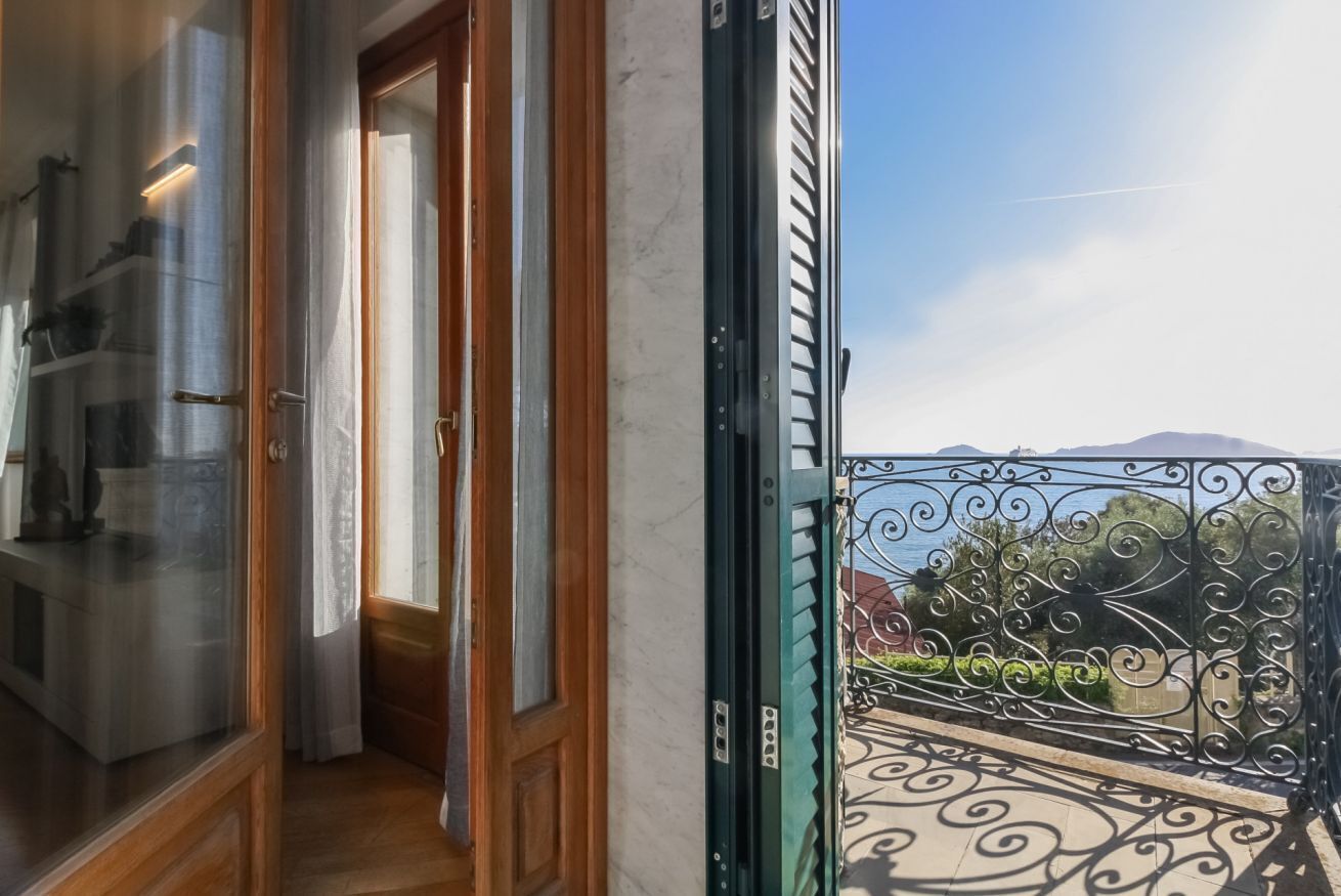 Un balcon doté d’une balustrade en fer forgé, d’une porte en bois et offrant une vue sur la verdure et les montagnes au loin.
