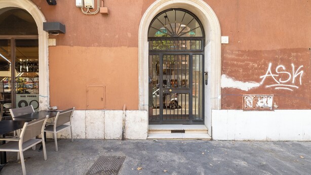 A building with a large arched entrance, a black gate, and a table with chairs outside. - Ostiensis Place, cozy accommodation in the heart of Rome, 9 minutes from metro B (Roma)
