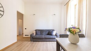 A modern living room with a grey sofa, a wooden dining table, and a vase of flowers. - Ostiensis Place, cozy accommodation in the heart of Rome, 9 minutes from metro B (Roma)