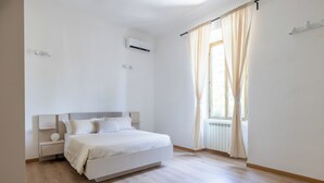 A minimalist bedroom with a bed, bedside tables, an air conditioning unit, and a window with curtains. - Ostiensis Place, cozy accommodation in the heart of Rome, 9 minutes from metro B (Roma)