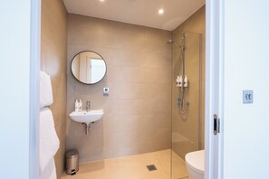 A modern bathroom with a glass-enclosed shower, a round mirror, a sink with toiletries, and a toilet. - Classic Two Bed (London)
