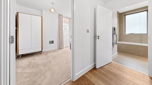 A modern room with a wooden floor, a white wardrobe, a ceiling light, and a large window. - One Bed Ground Floor (London)
