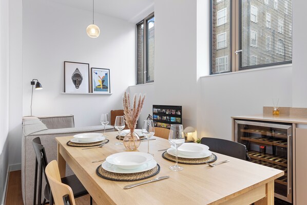 A dining area with a wooden table set for four, a wine cooler, and artwork on the walls. - Split Level Apartment (London)