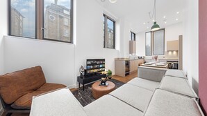 A modern living room with a sofa, a coffee table, and a TV. There is a kitchen area in the background. - Split Level Apartment (London)
