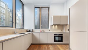A modern kitchen with white cabinetry, a wooden floor, and a window with blinds. - Split Level Apartment (London)