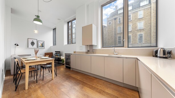 A modern kitchen with a wooden dining table, white cabinets, and large windows. - Split Level Apartment (London)