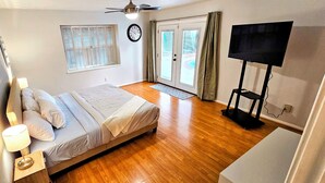 A bedroom with a bed, a TV, a window with blinds, a door, and a wall clock. - Spacious 4-bedroom 2-bath POOL HOUSE fully fenced (Spring)