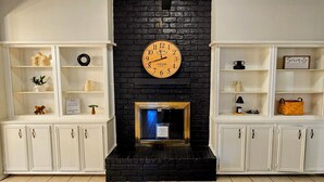 A room with a black brick fireplace, white shelving units, and a clock above the fireplace. - Spacious 4-bedroom 2-bath POOL HOUSE fully fenced (Spring)