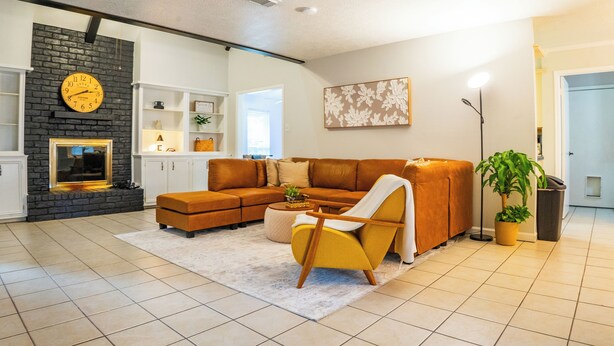 A modern living room with a sectional sofa, a yellow armchair, a fireplace, and a large clock on the wall. - Spacious 4-bedroom 2-bath POOL HOUSE fully fenced (Spring)