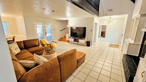 A living room with a brown sofa, a yellow armchair, and a TV. There is a staircase leading to another level. - Spacious 4-bedroom 2-bath POOL HOUSE fully fenced (Spring)