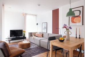 A modern living room with a sofa, TV, and a dining area with a table and chairs. - Superior Two Bed (London)