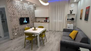 A modern living room with a grey sofa, yellow cushion, and a dining area with a white table and yellow chairs.