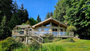 Ein zweistöckiges Holzhaus mit einem Balkon, umgeben von üppigem Grün und Bäumen.