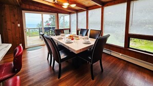Ein Essbereich aus Holz mit Tisch für vier Personen, großen Fenstern und Blick ins Freie.