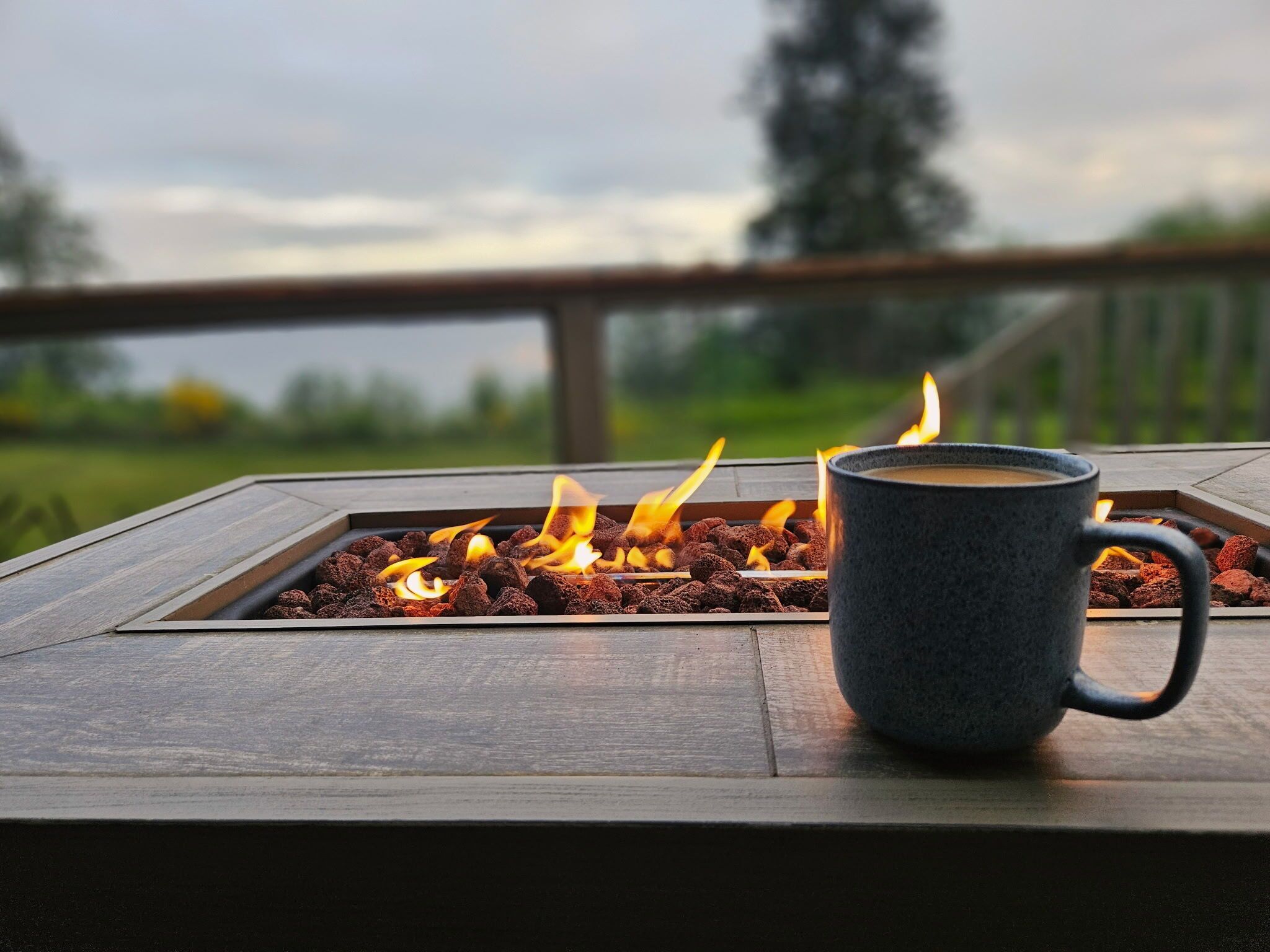 Un brasero con leña ardiendo y una taza sobre una mesa de madera.