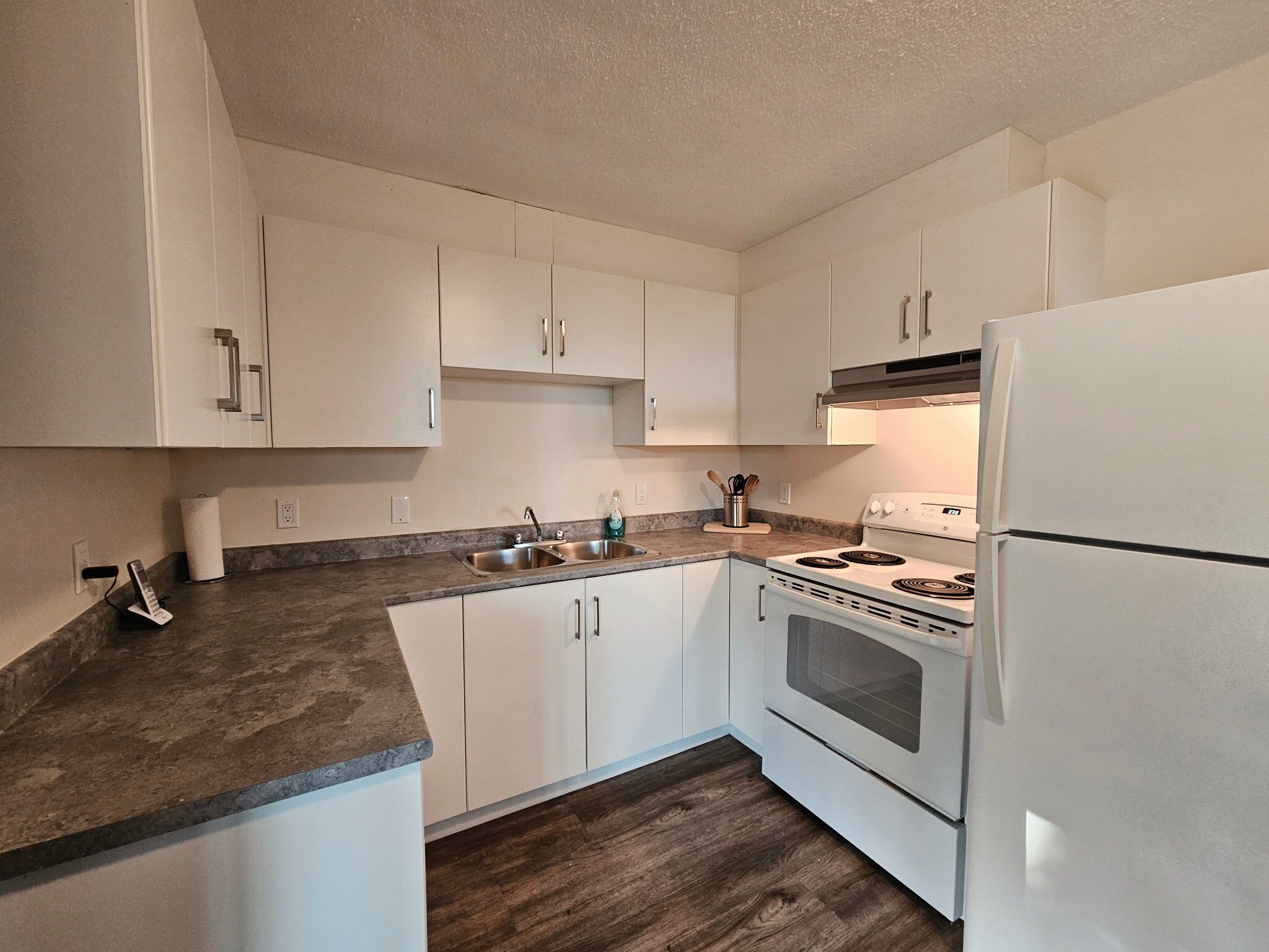 A kitchen with white cabinets, a stainless steel sink, a stove, and a refrigerator.