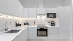 A modern kitchen with white cabinetry, stainless steel appliances, and under-cabinet lighting.